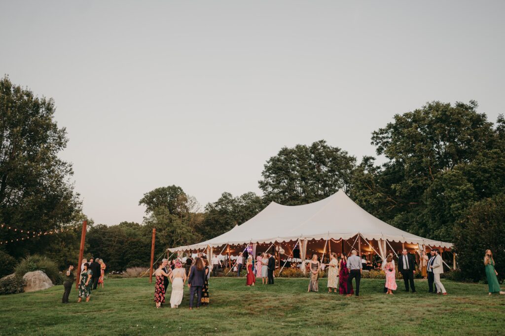 Reception tent in the grass surrounded by lush trees.
