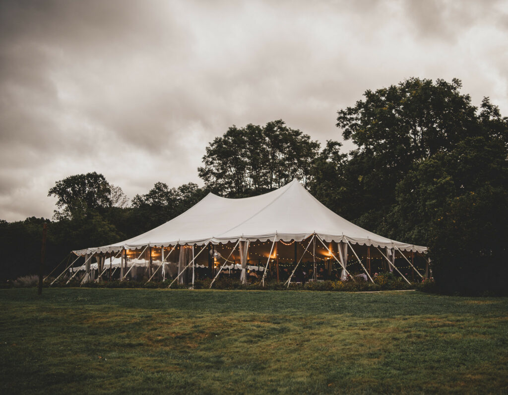 Reception tent in the grass in front of large trees.