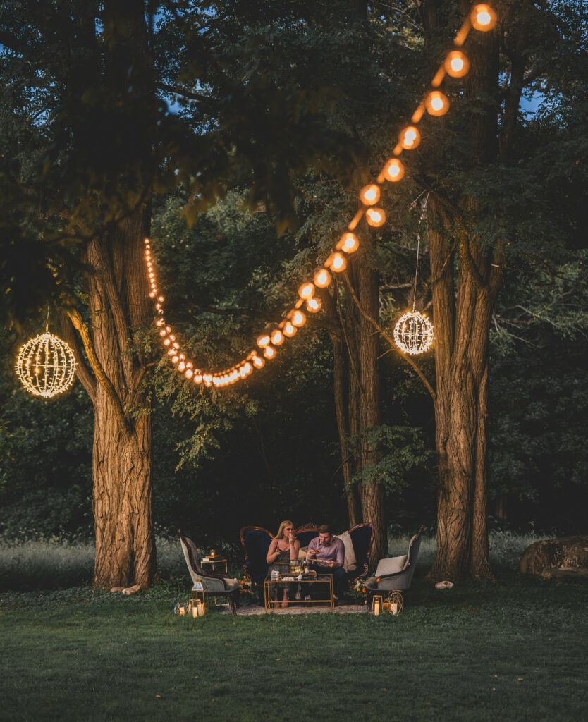 Seating lounge set under glowing lights and tall trees.