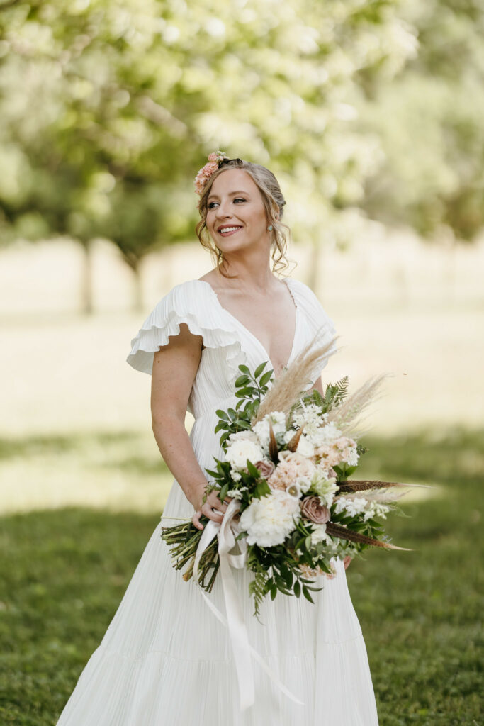 Bride in field hold bouquet.