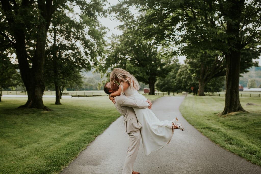 Grooms lifts bride in the air on a walking path.