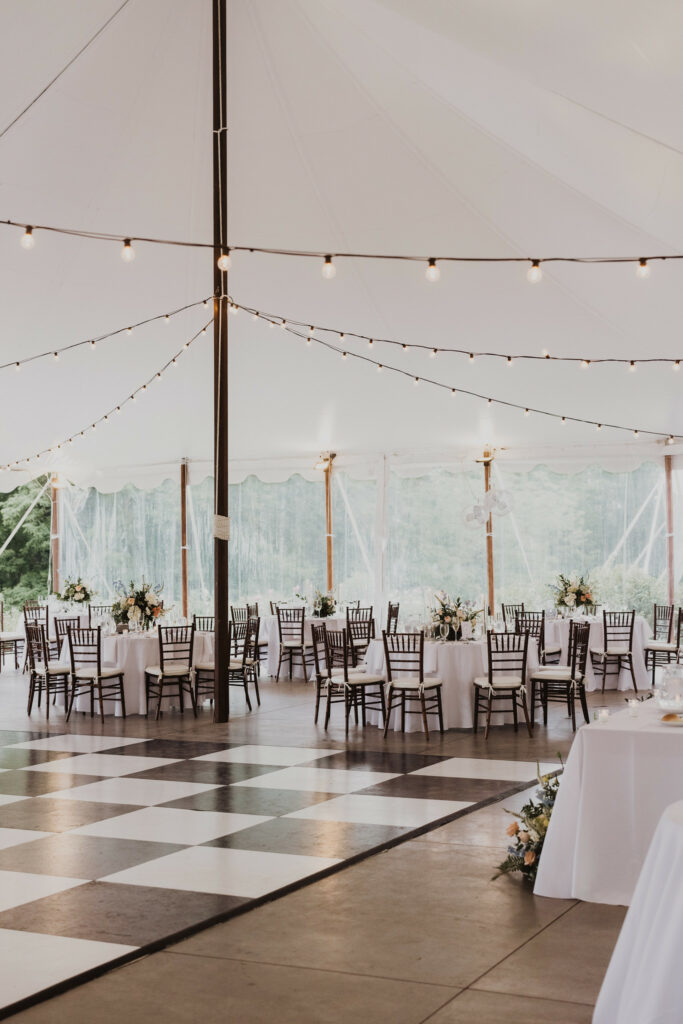 Under the reception tent shimmering lights are strung over a checkered dance floor and dinner tables.