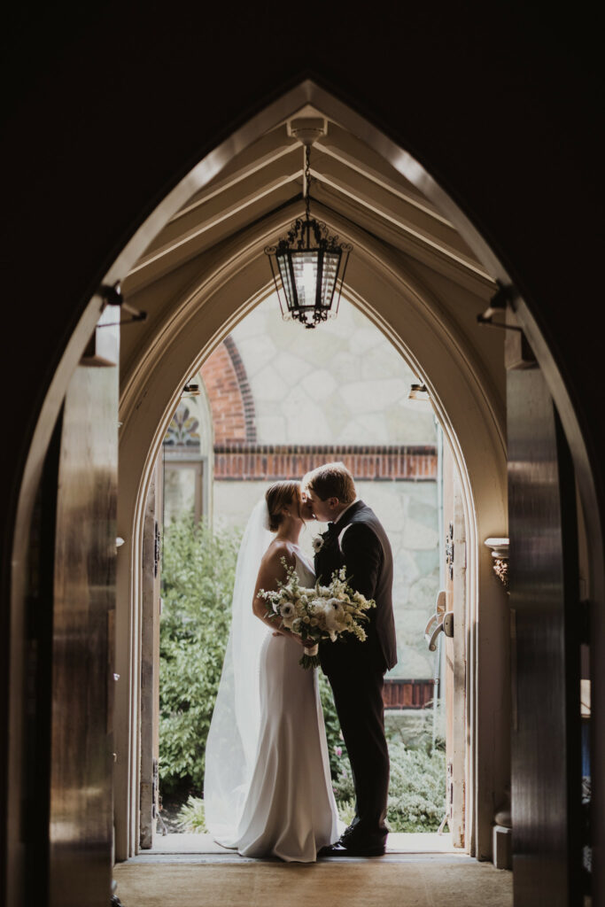 Newlyweds embrace under a doorway with a kiss.