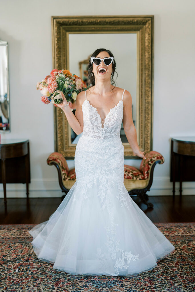 Bride posing laughing with heart shaped sunglasses holding her bouquet.
