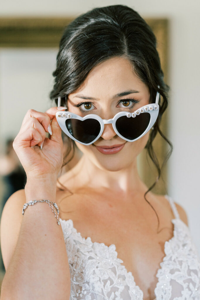 Bride pulling her heart shaped sunglasses down her nose and smirking at the camera.