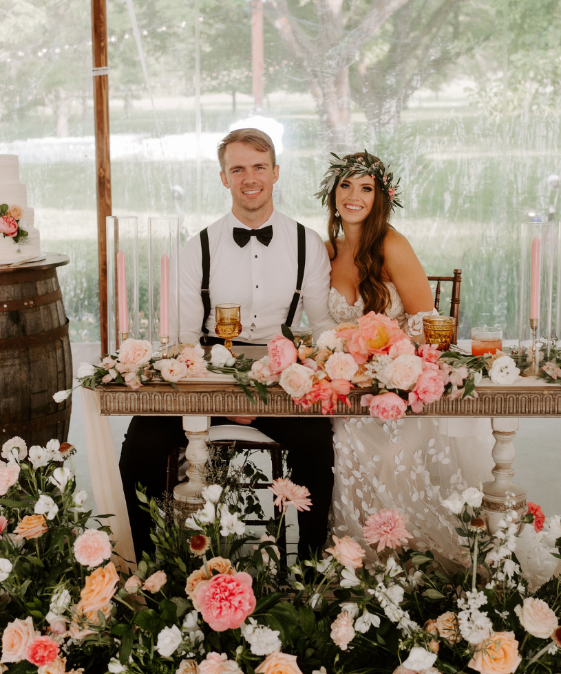 wedding couple smiling at a headtable with colorful flowers