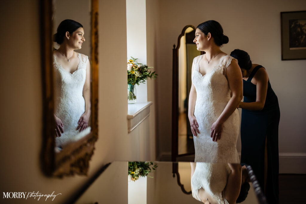 Helping bride put on her wedding dress in front of a mirror in a private wedding suite at Springton Manor Farm