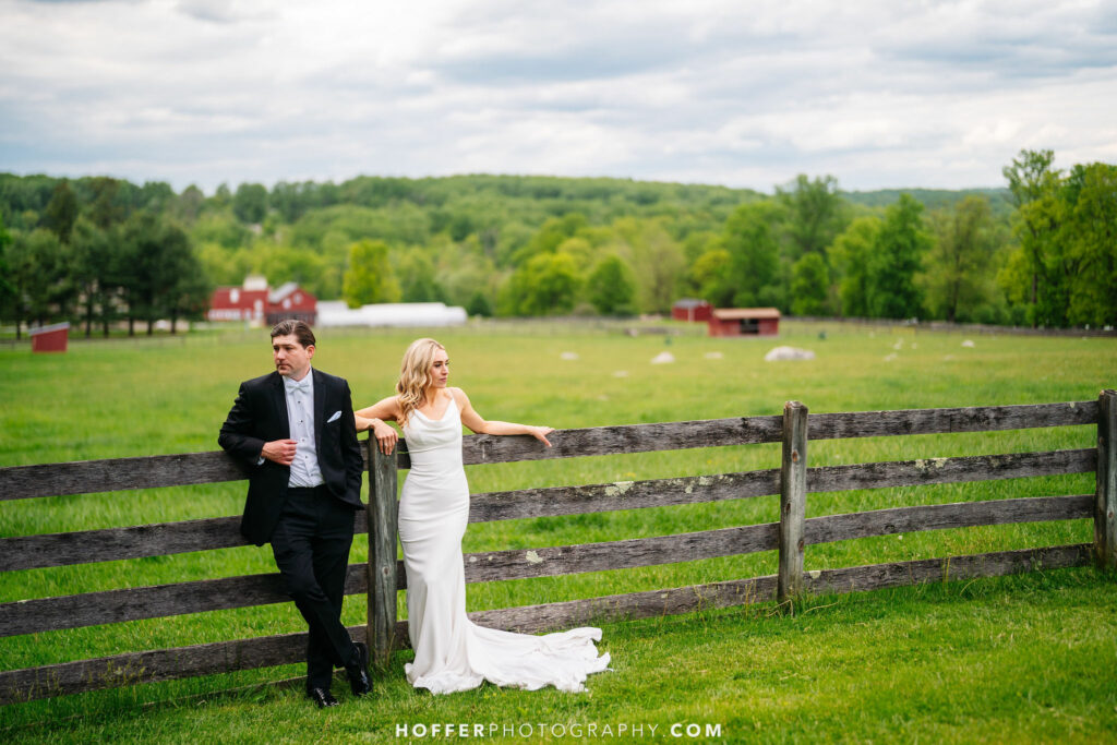 Newlyweds standing against the farm fence.