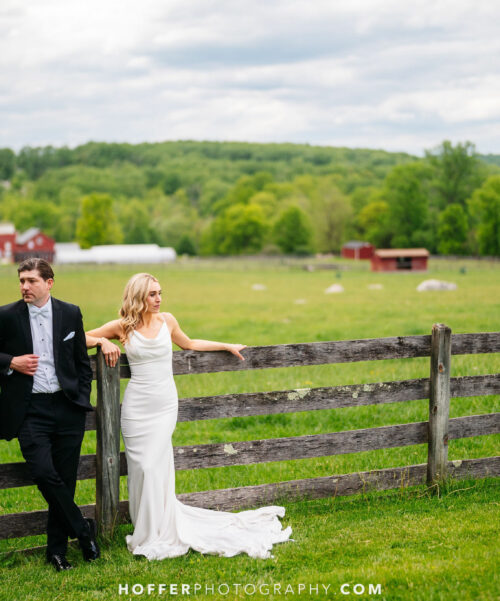 Newlyweds standing against the farm fence.