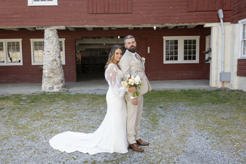 Couple posing in front of dark old red barn.