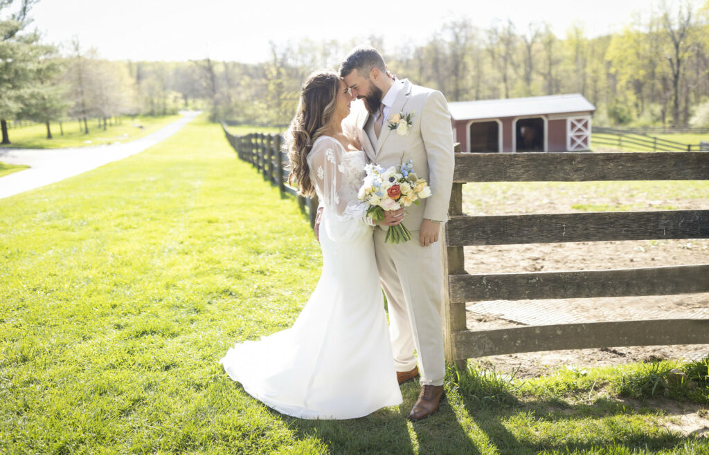 Newlyweds standing in front of farm fence.