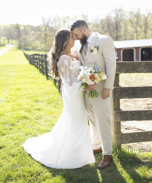 Newlyweds standing in front of farm fence.