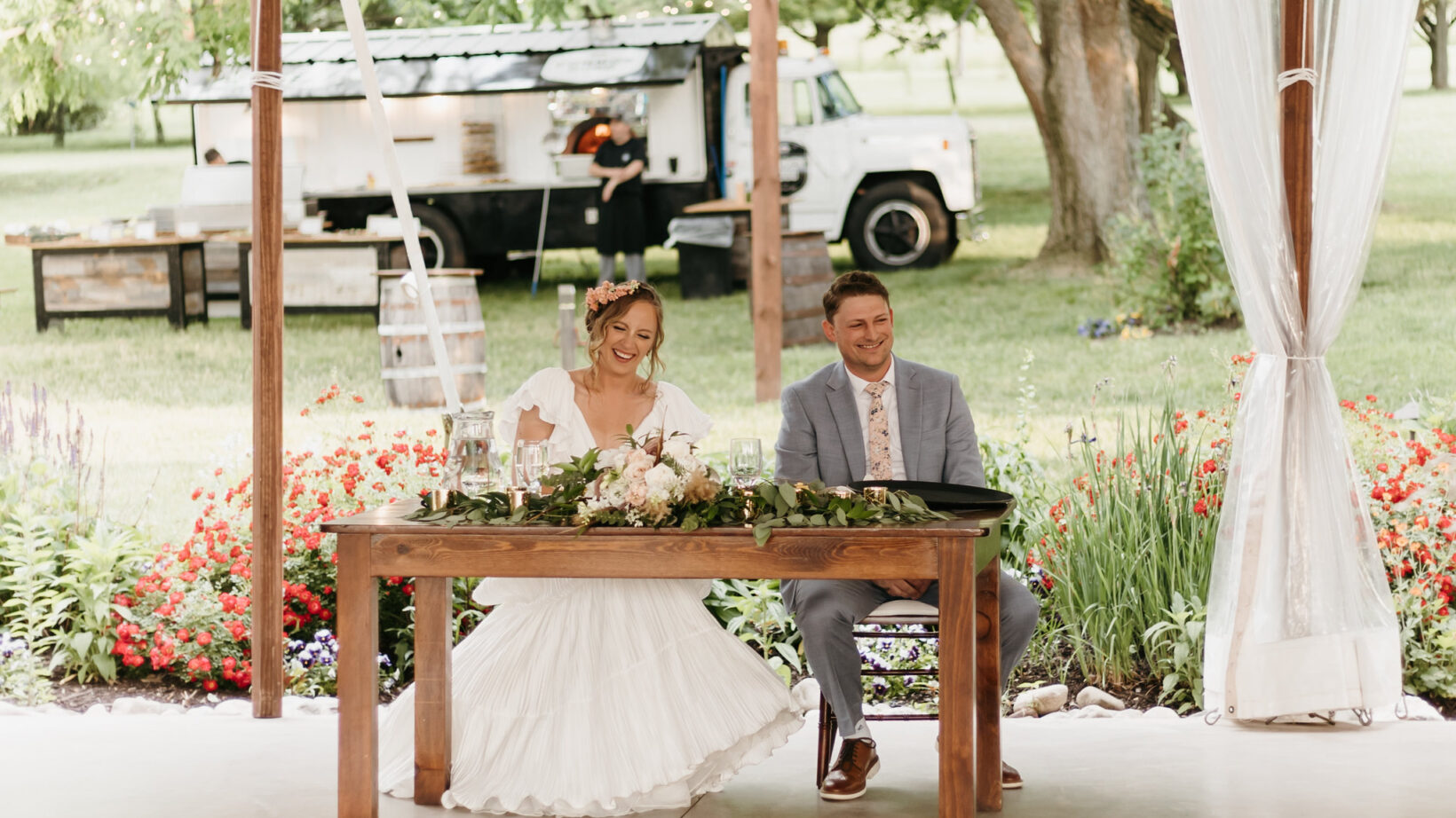 Bride and groom at sweetheart tbale with Common Good Pizza Food Truck in the background